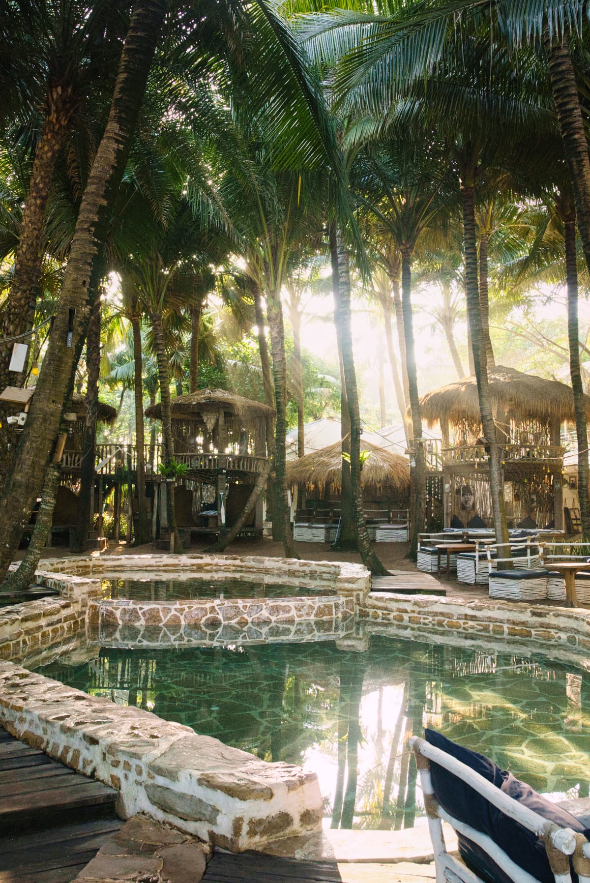 Rustic stone pool surrounded by daybeds and palms at a beach club in Canggu, Bali