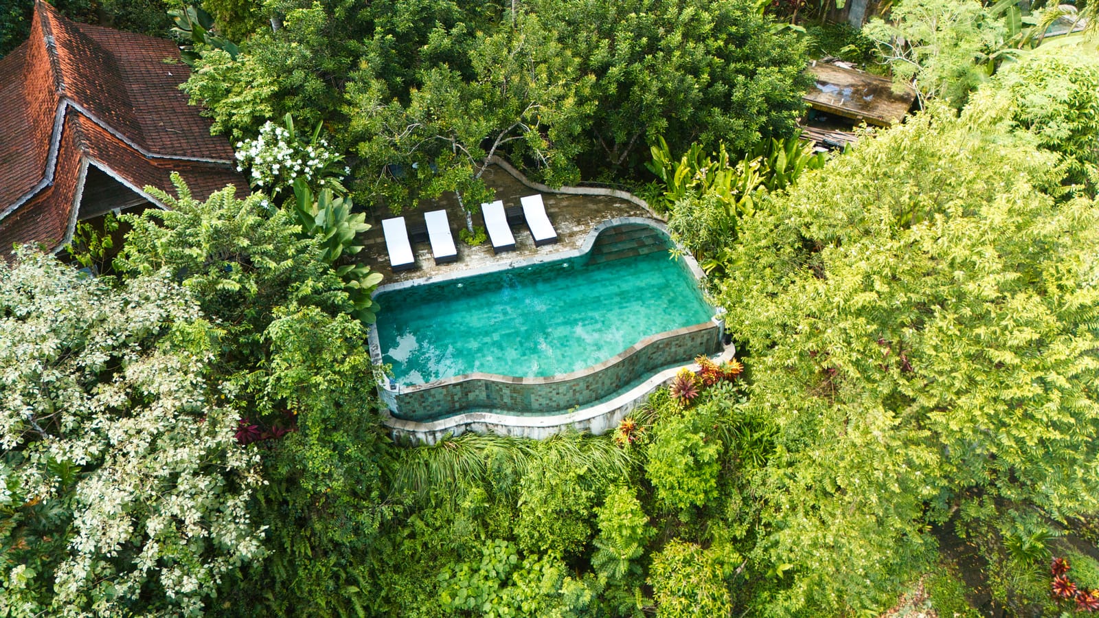 Aerial view of an infinity-edge pool spilling toward a lush green jungle valley in Bali